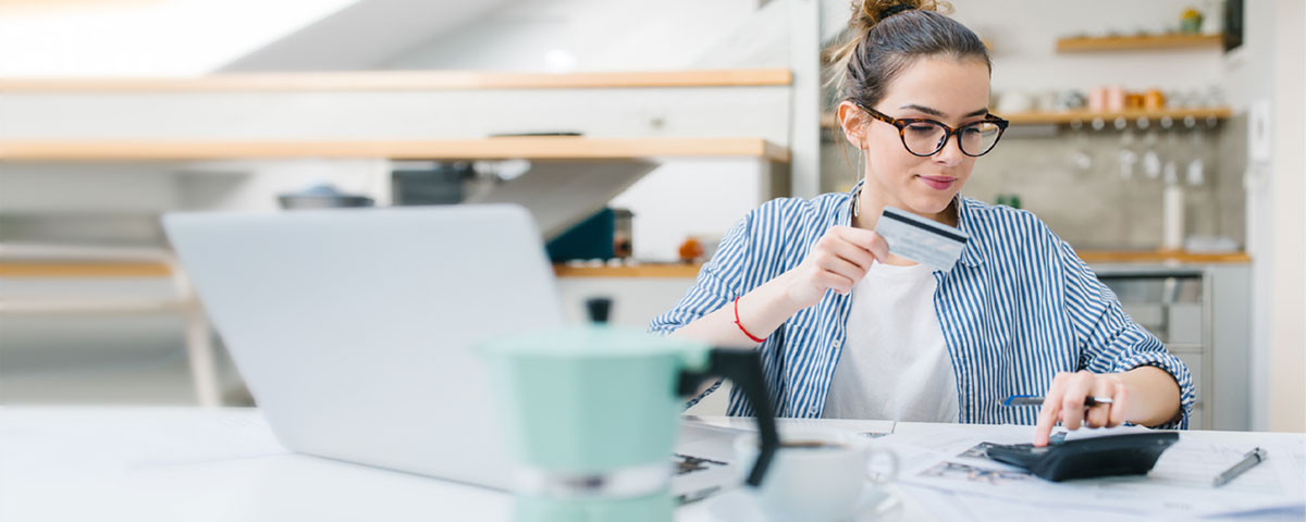 Woman using calculator and bank card surrounded by financial documents to keep track of her business finances 