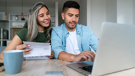 A man and woman smile as they progress an application on a laptop, representing positive outcomes for borrowers with NatWest Business.