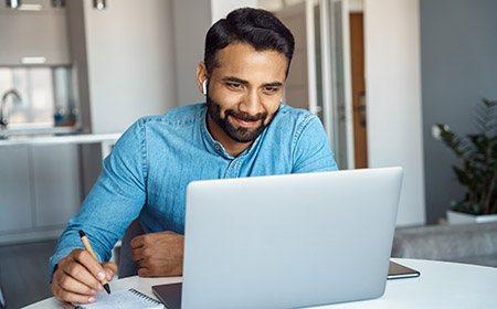 A man smiles, working at a laptop from home, signifying good investment outcomes, supported by NatWest commercial mortgages.