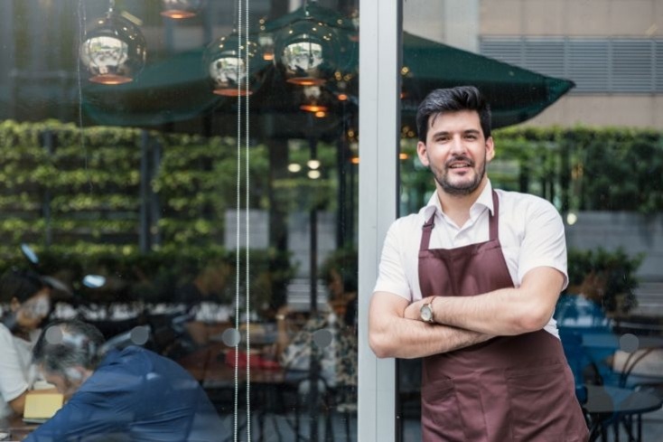 A restaurateur smiles as he stands outside his business premises, conveying successful, quick lending decisions from NatWest Business.