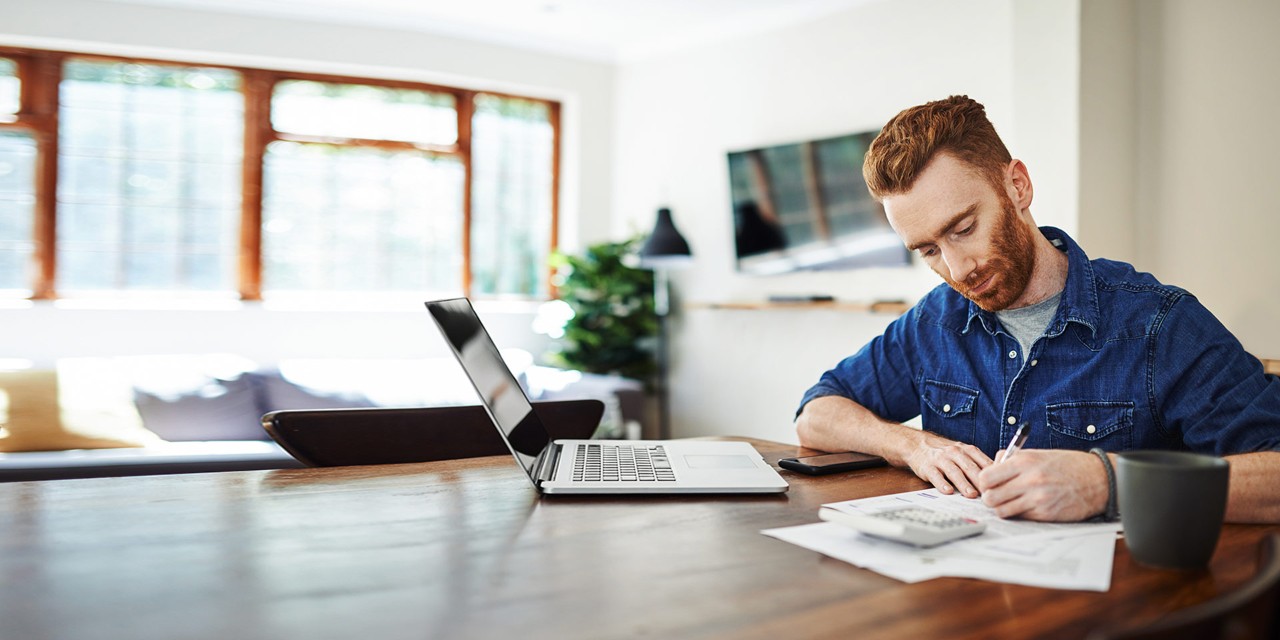 White ginger bearded man working out finances at a desk near laptop