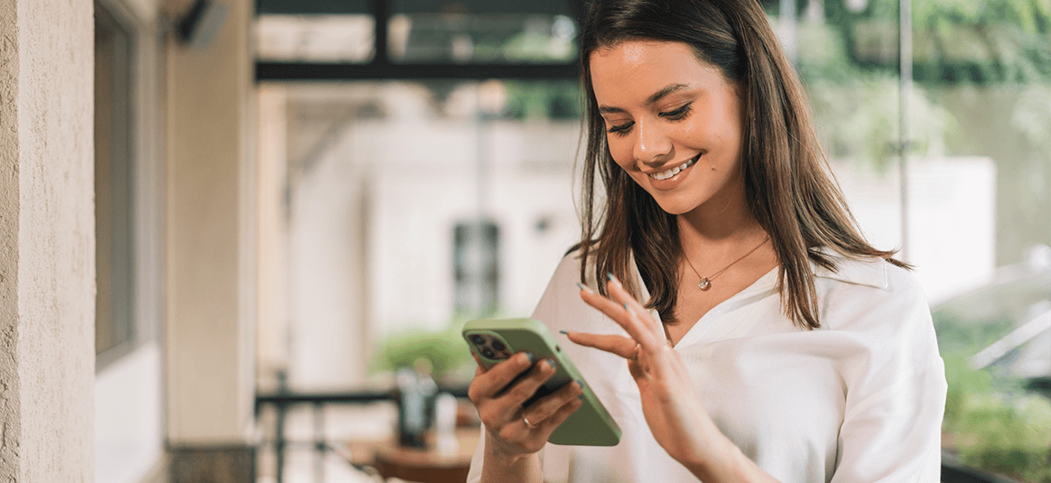 A woman is using her mobile phone, smiling, relaxed, representing how using biometric approval with NatWest business banking keeps customers happy and safe.