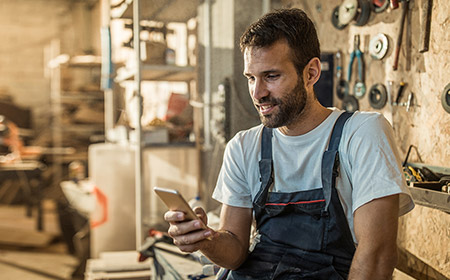 Photo of smiling man looking at phone in a workshop