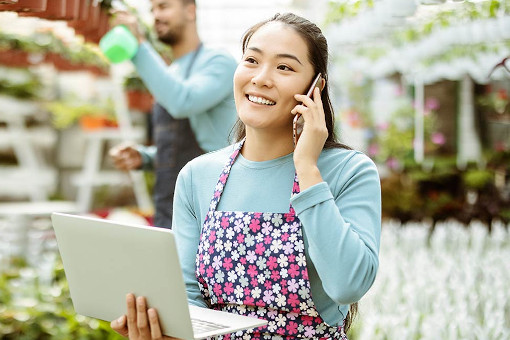 Person in an apron using a laptop in a greenhouse.