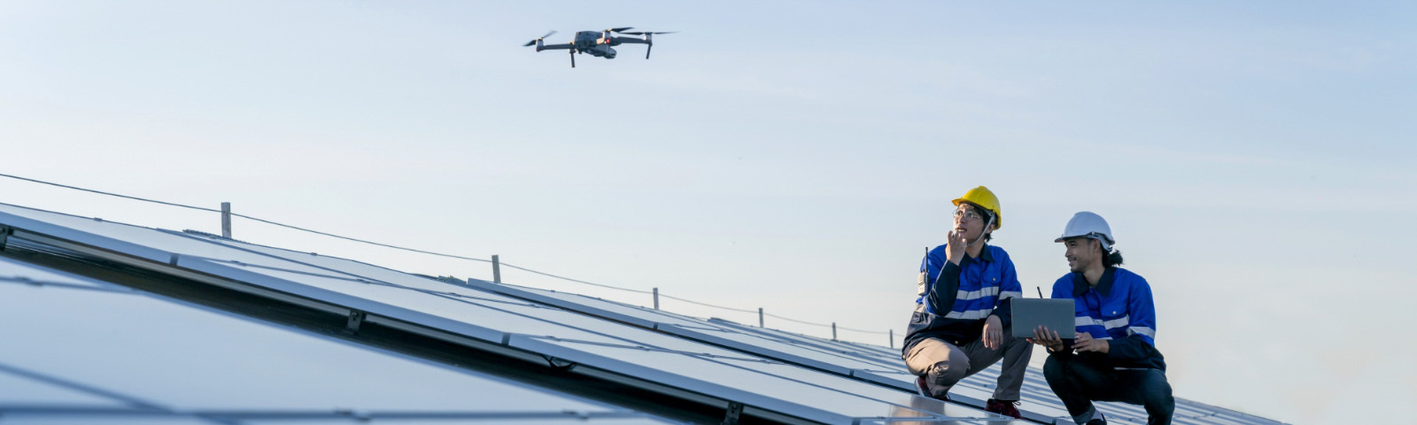Two workers on a solar panel roof looking a drone