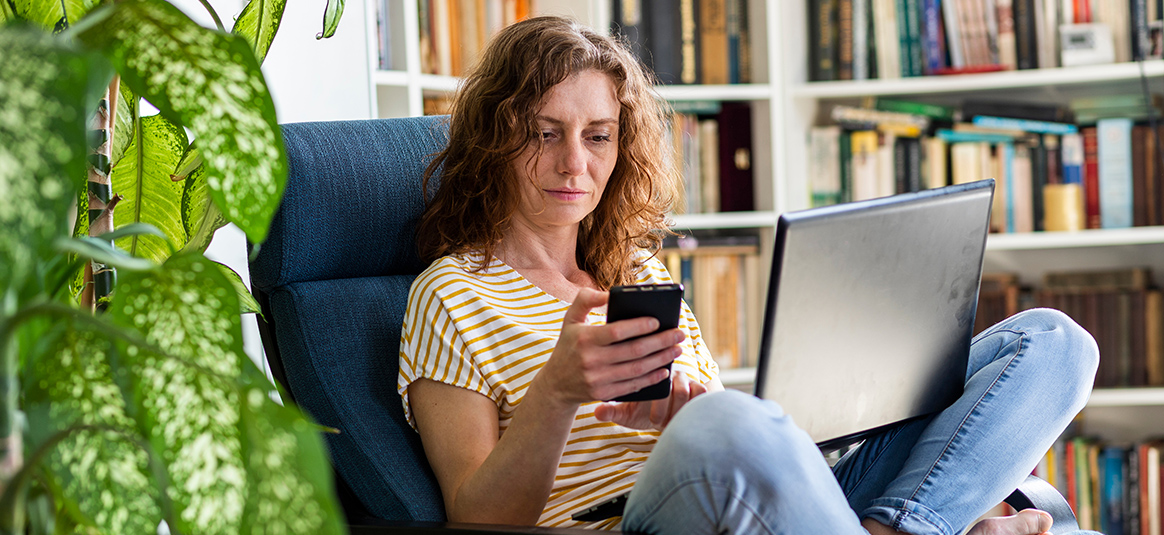Woman sitting cross legged with laptop in lap and phone in hand