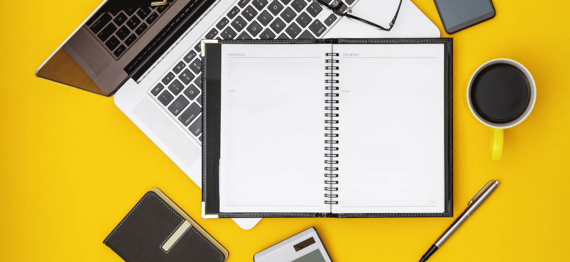 Photo of a notebook, pen, laptop and coffee cup on a yellow background