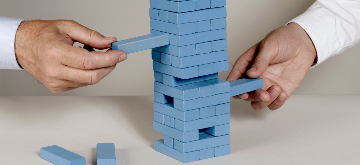 Photo of two hands pulling out blue bricks from a Jenga tower