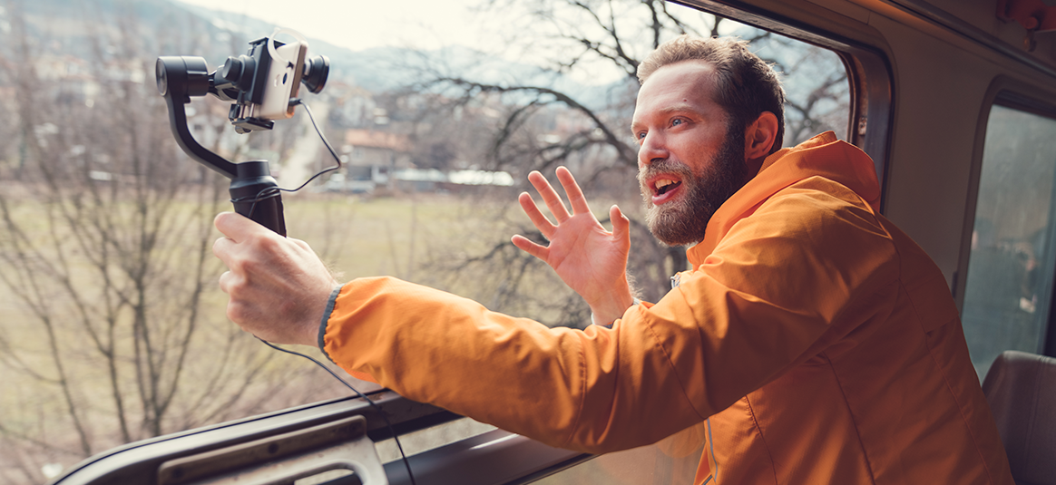 Photo of a man in an orange jacket holding a camera mounted on a selfie stick