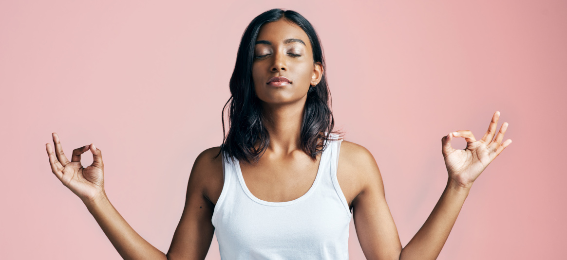 Photo of a woman meditating in front of a pink background