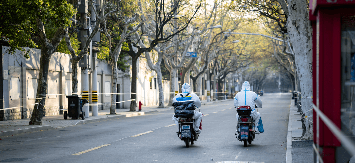 Photograph of 2 people riding mopeds dressed in PPE in empty road