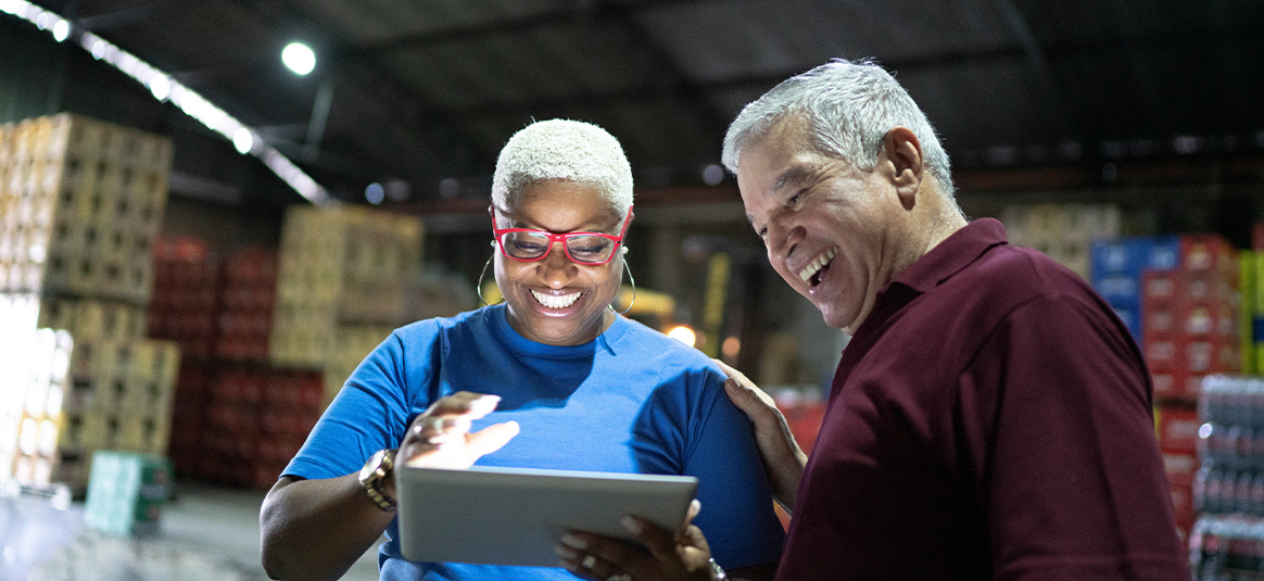 Photo of two smiling people in a warehouse looking at a tablet