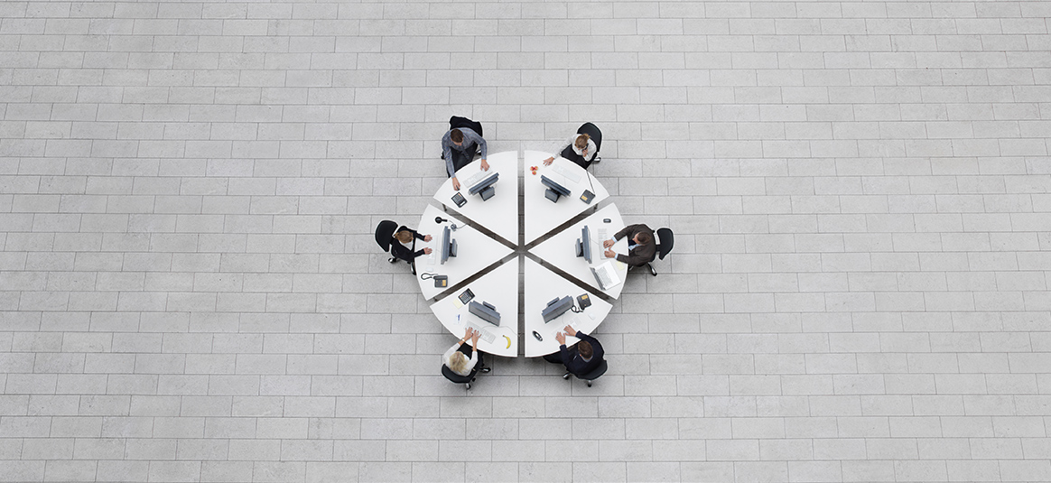 An aerial view of six office workers working around a circular table