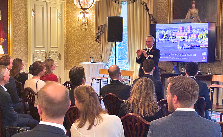 Audience seated facing a speaker with a presentation screen in the background