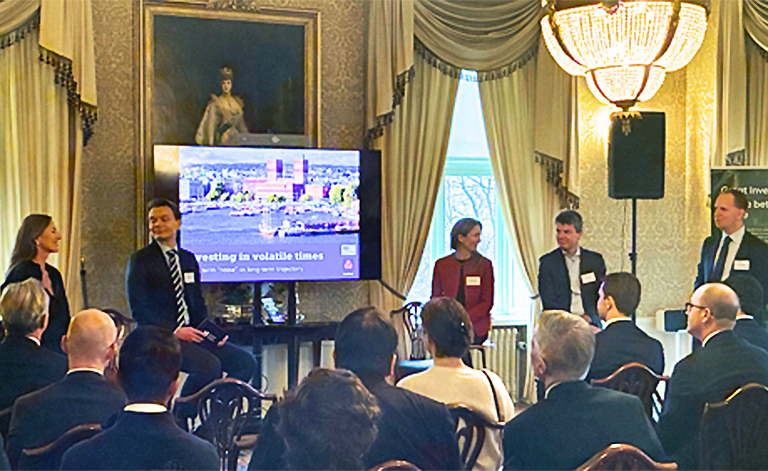 Audience seated facing 5 speakers with a presentation screen in the background