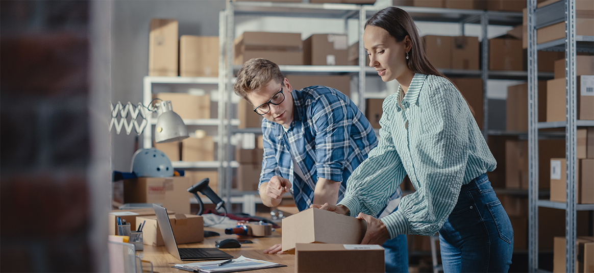 Picture of a man and Woman working in a warehouse looking at a cardboard box