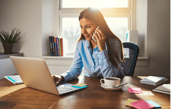 Photo of woman working at laptop and holding mobile phone