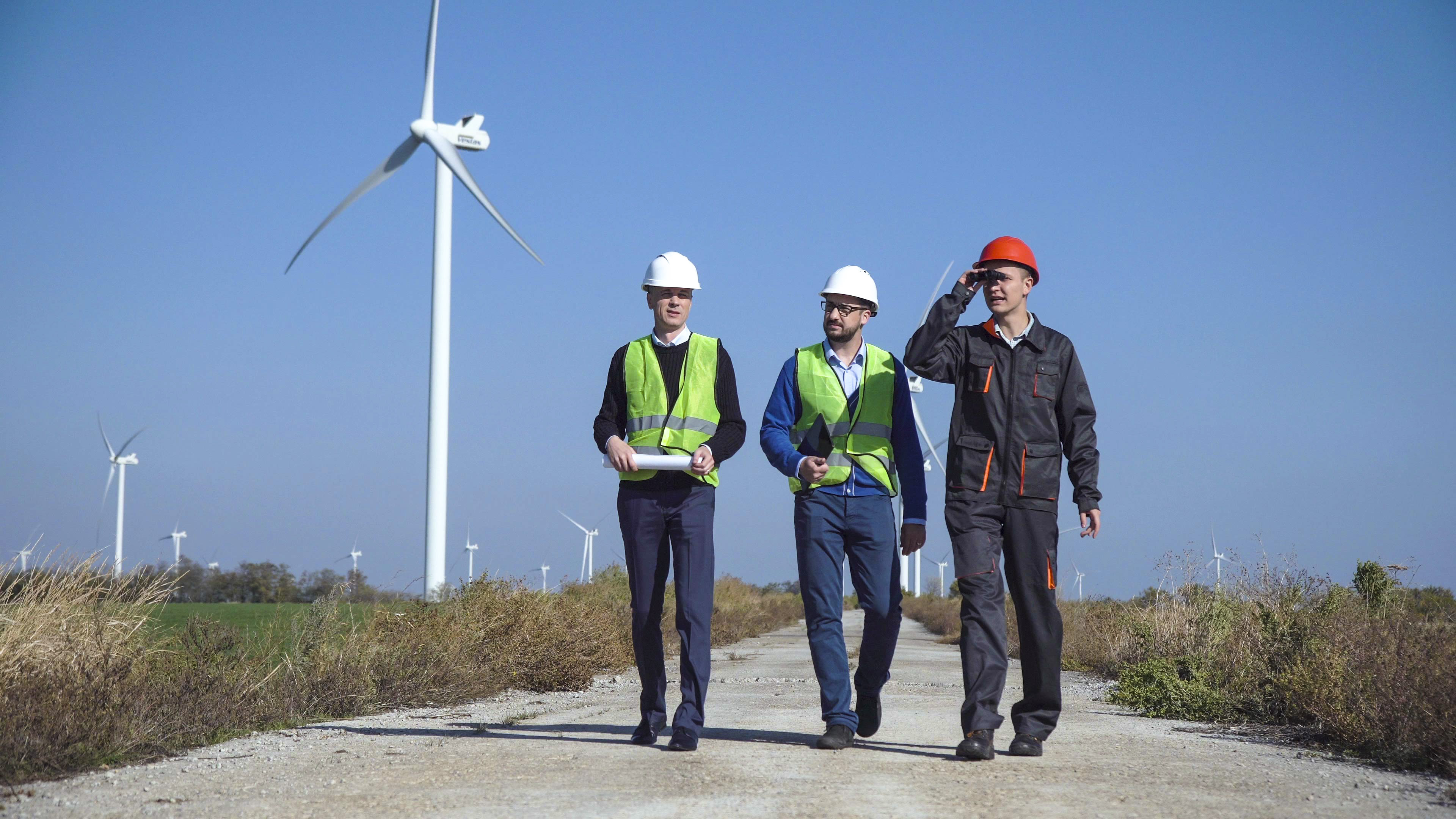 Three men in hard hats walking by some windmills
