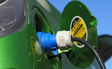Photo of a green car with connected charging cable.