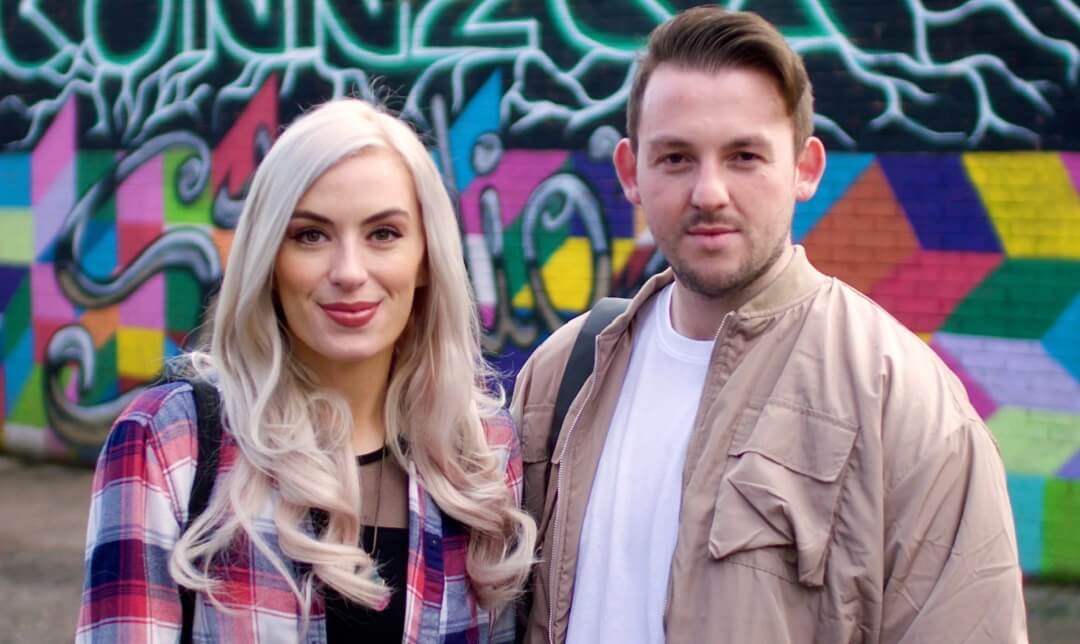 Photo of a young man and woman standing in front of a graffitied wall