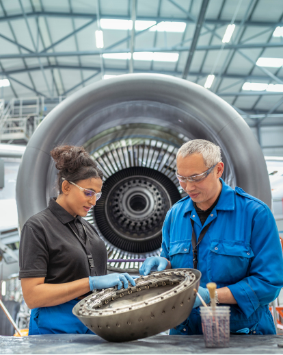 A male and a female engineer, standing in front of a plane turbine and fixing mechanics.