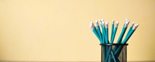Photo of several blue pencils in a pot against a beige background