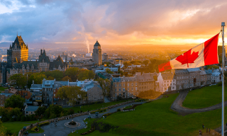 View of Québec skyline and low sunlit horizon beyond, with Canadian flag flapping in the foreground.
