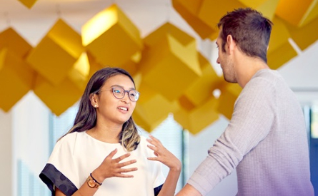 Photo of two people talking in front of hanging yellow cubes