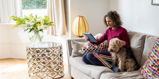 Woman sitting on the sofa with her dog whilst using her tablet