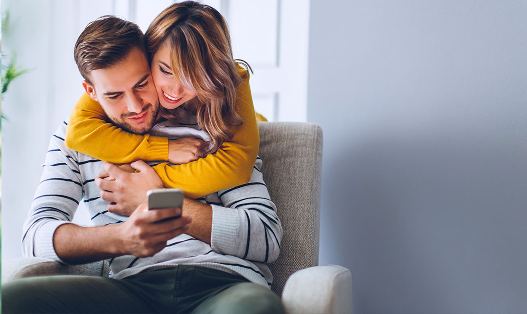 Couple hugging at home using mobile device