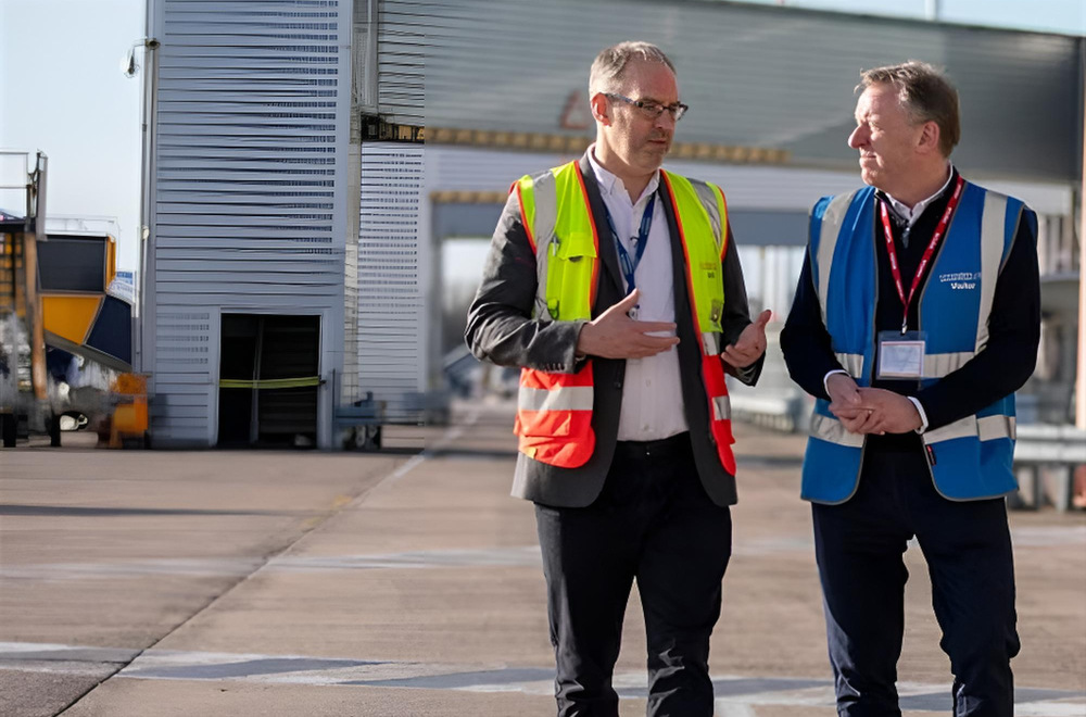 Two men wearing hi vis jackets and talking whilst walking around in an airport, showing the support NatWest group has of infratsructure businesses.