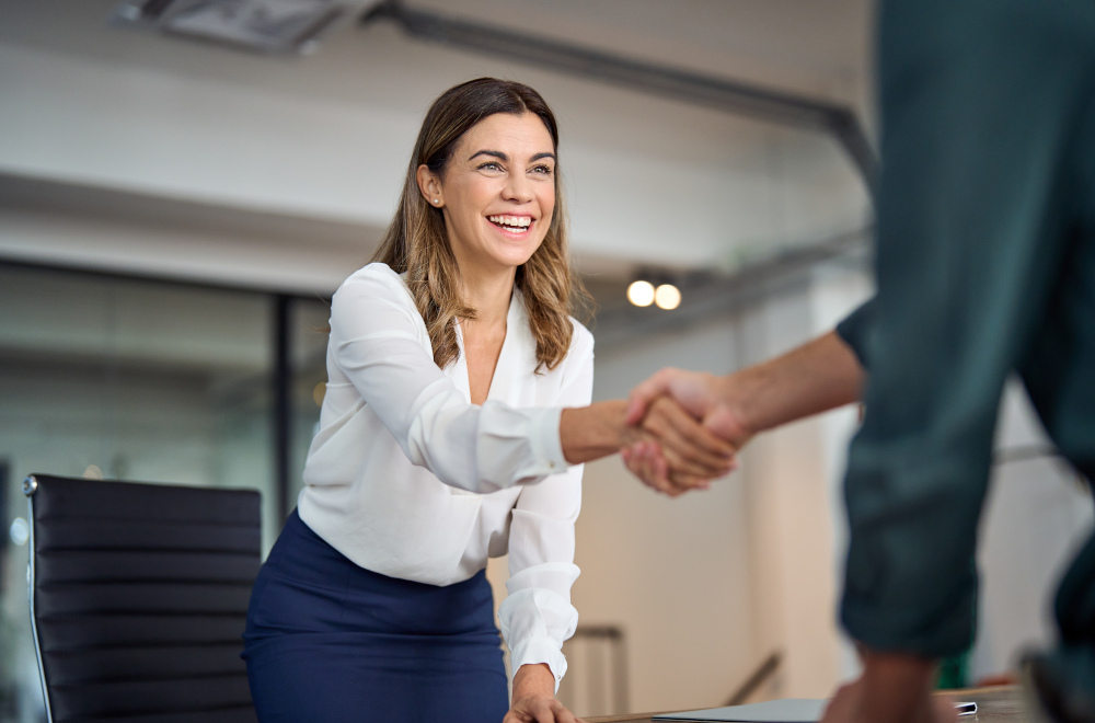 Smiling woman in an office shaking hands with someone off camera.