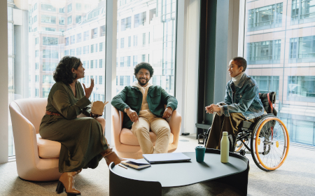 Two people sitting in armchairs and one in a wheelchair. All are in an office building.