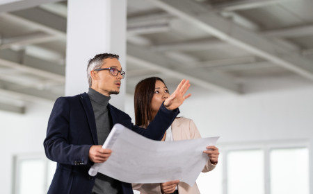 Two people standing in an empty office and looking at a blueprint on a large sheet of paper.