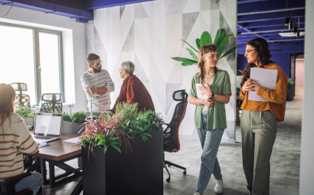 A modern looking office environment with five employees wearing casual clothes and chatting to each other. 