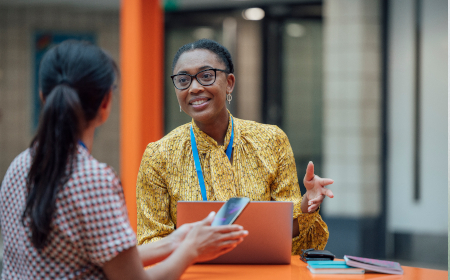 Two professionally dressed women in an office environment talking to each other.