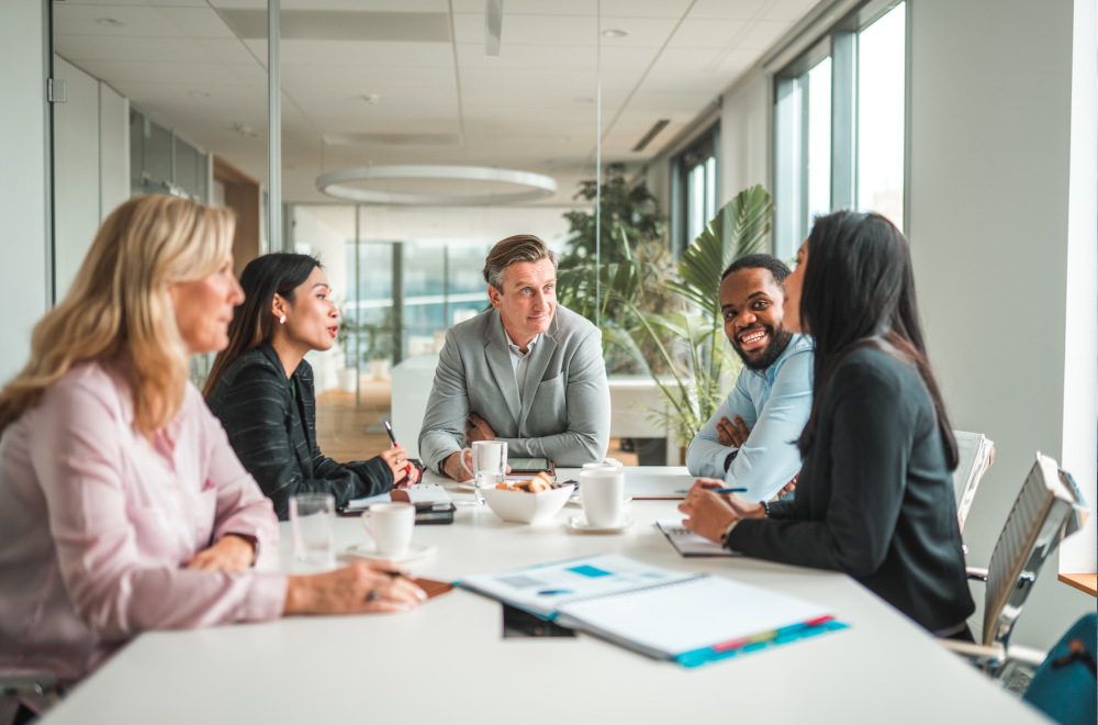 Five professionals in an office environment and sat at a table having a meeting.