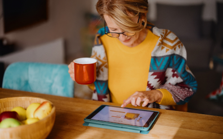 Woman holding a mug of tea whilst interacting with her tablet.
