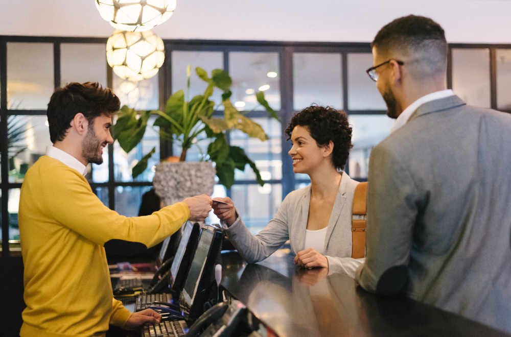 A man and a woman paying a receptionist in a hotel lobby.