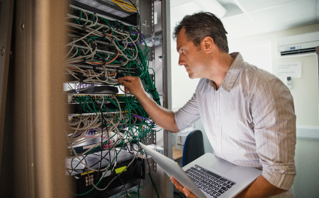 Man in a server room managing network cables while holding a laptop