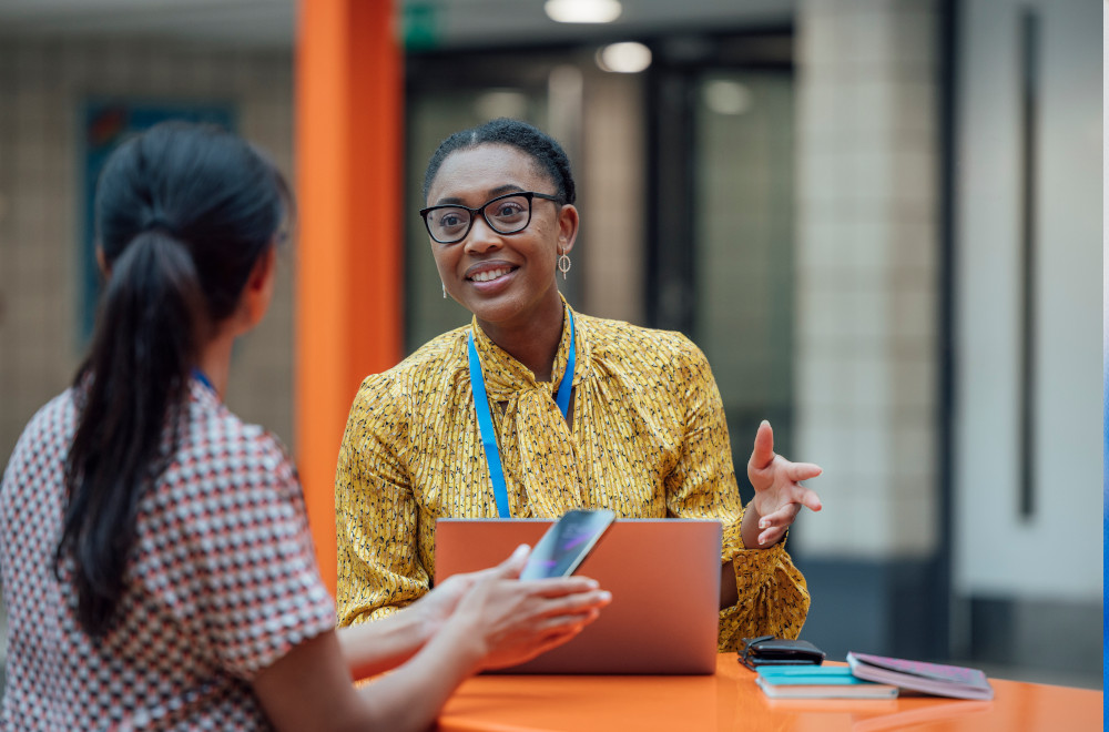 Smiling professional woman sitting at a desk with a laptop, engaged with a client