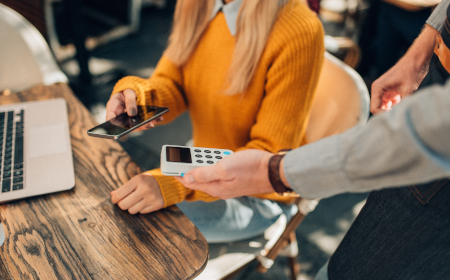 A hand holding a card machine out for a customer who is using their phone to pay.