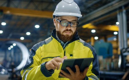 A man in a hard hat looking at information on a tablet.