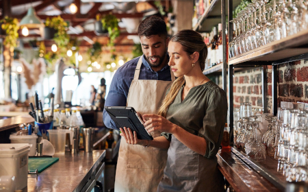 Two employees behind a bar in a restaurant looking at a tablet. 