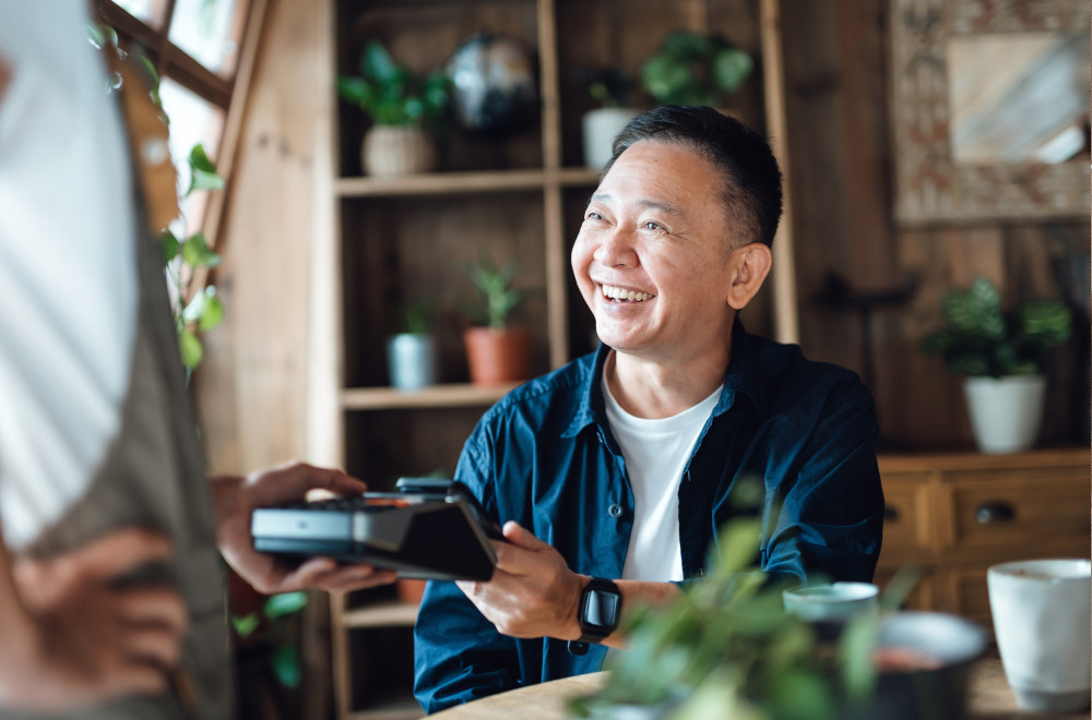 Smiling man completing a payment with a commercial credit card at a point-of-sale terminal.