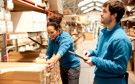 Two people wearing uniforms in a warehouse standing by neat stacks of cardboard boxes.