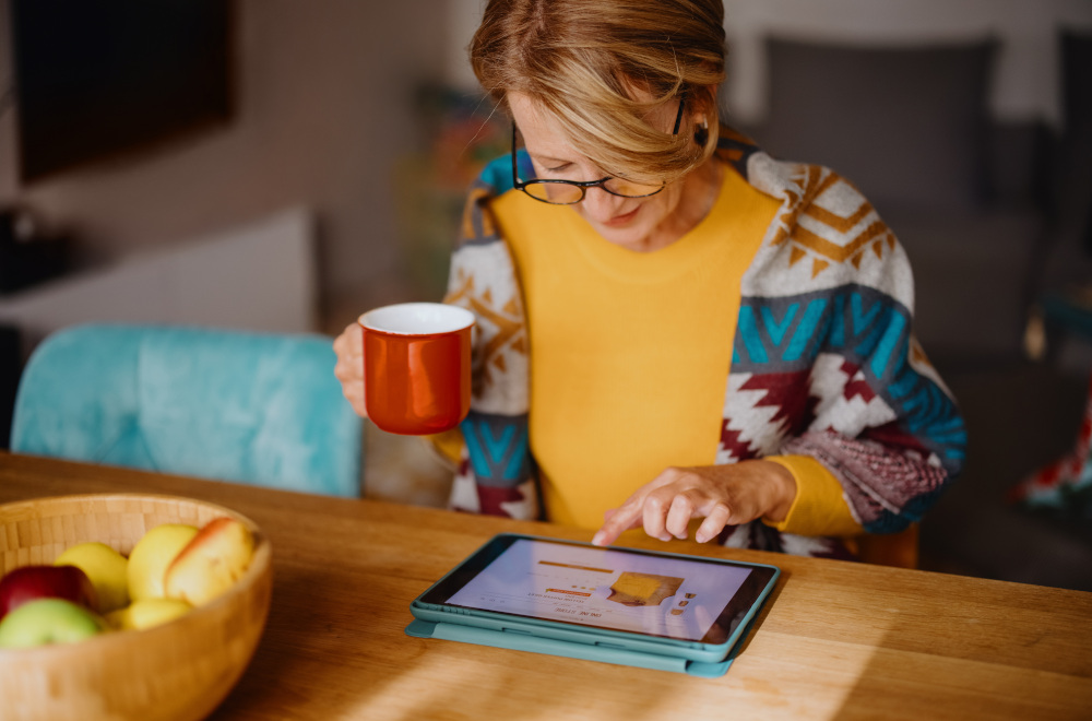 A woman holding a mug and looking at data on a tablet.