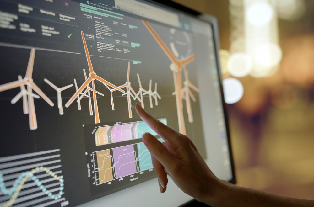 A hand pointing at a screen displaying images of wind turbines.
