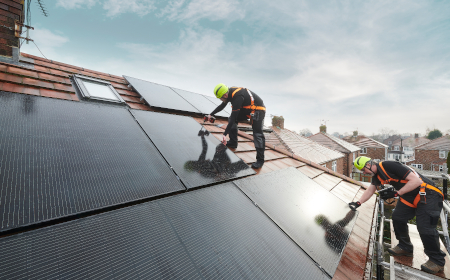 Two construction workers wearing hi vis jackets and hard hats installing solar panels onto a roof.