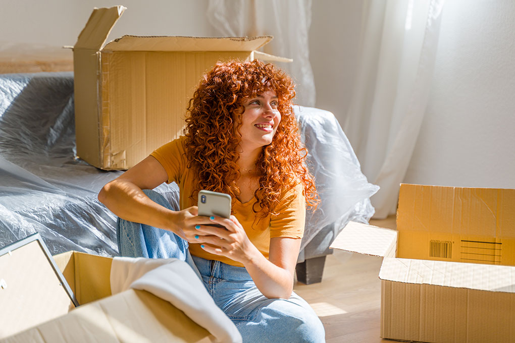 Young woman sitting in her bedroom on her app after moving